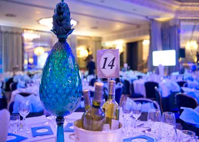 A table dressed in blue and white tablecloths featuring a vase containing a pineapple centerpiece at the sbid awards in London.