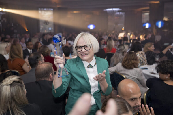 A lady wearing a green jacket holding up a trophy at the 2018 sbid awards.