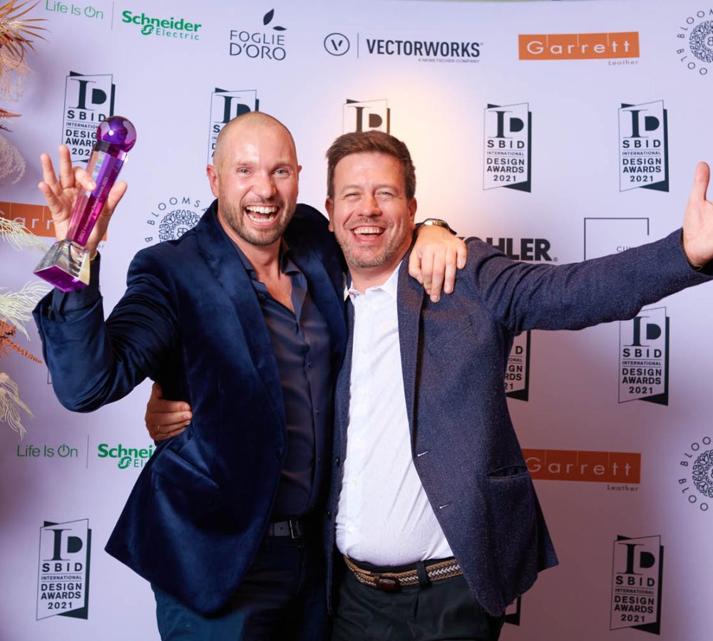Two men celebrating at the SBID Awards 2021, posing for a photo with their hands raised in excitement.